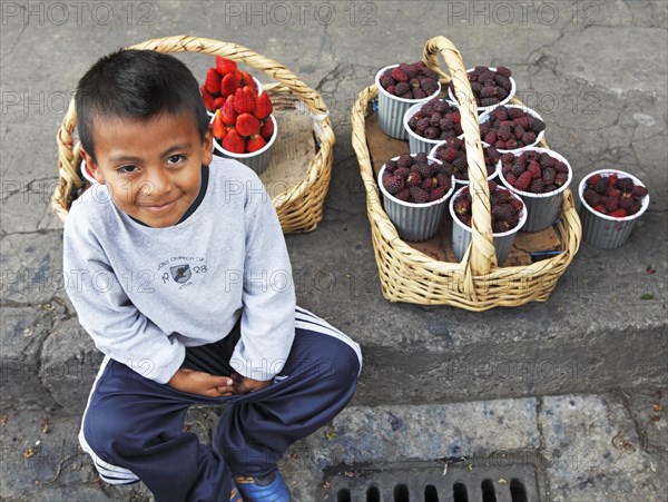 Boy with fruit punnets sitting on the curb of a street