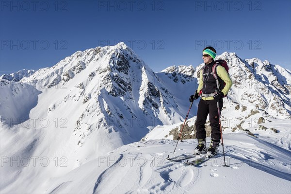 Ski tourer on the summit of Mt Seespitz in the Deutschnonsberg area with the mountains Illmenspitz and Proves at the back