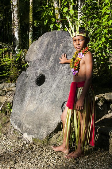 Traditionally dressed boy standing in front of stone money