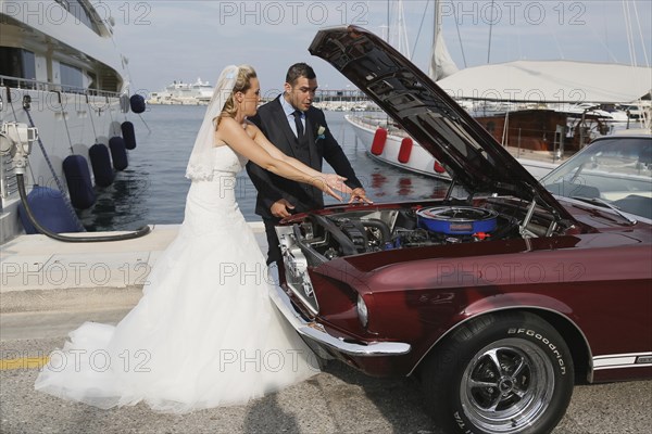 Bride and groom looking into the engine compartment of a Ford Mustang after a breakdown