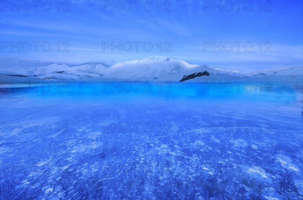 Monte Vettore at blue hour with a frozen puddle with air bubbles