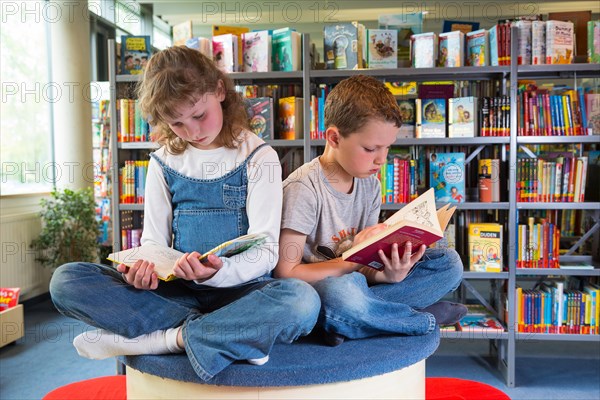 Two children reading reading books in a public library