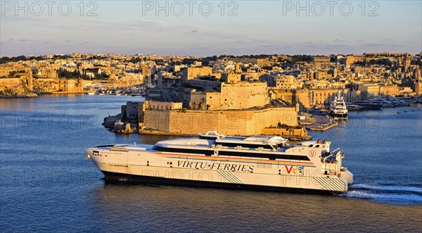 Jean de la Valette ferry of the Virtu Ferries shipping company passing the fortress Fort St. Angelo in the Grand Harbour