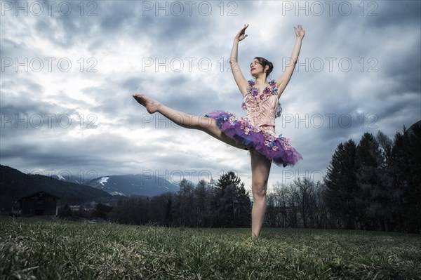 Ballerina wearing a tutu dances in front of a cloudy