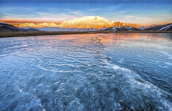 Monte Vettore in the evening light with a frozen puddle with small waves