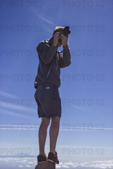 Young man taking a photo whilst standing on a rock