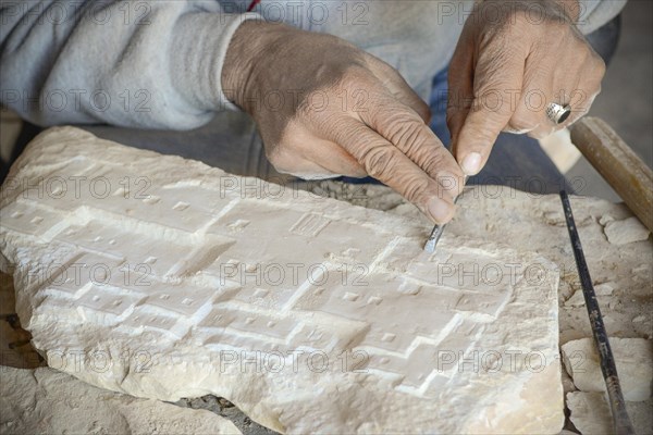 Man carving model of house on stone