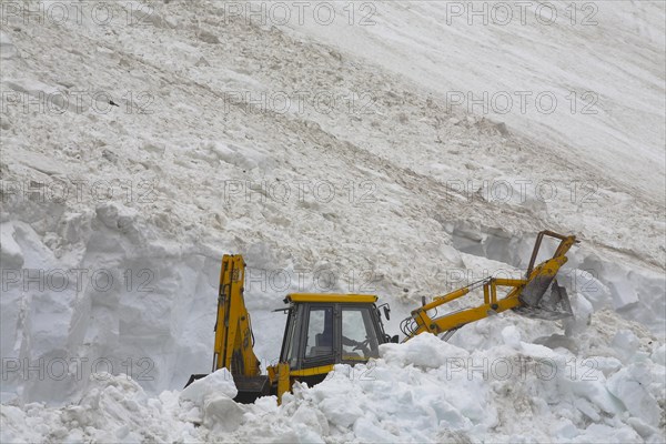 Excavator shovelling away the snow of an avalanche