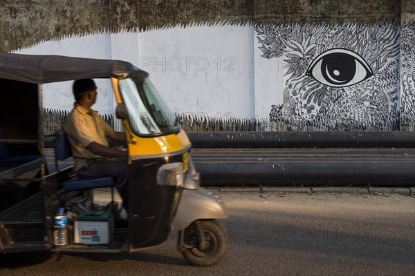 Rickshaw driver looking at graffiti on a wall in Kochi