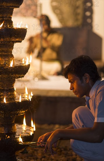 Young man lighting oil-soaked wicks on a stone chandelier