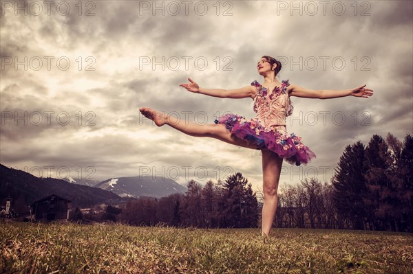 Ballerina wearing a tutu dances in front of a cloudy sky