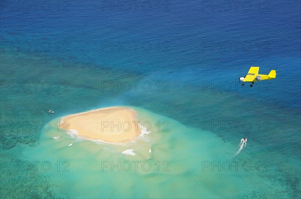 Small plane flying over coral reef with sand island