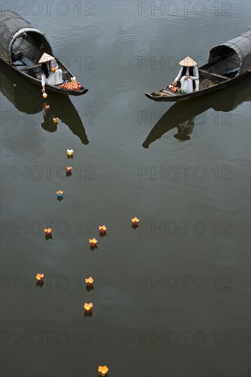 Two women in Ao dai robes put floating candles on water