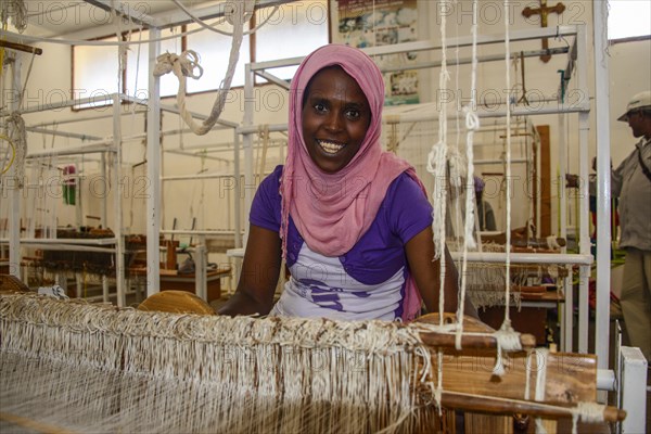 Friendly woman working on a hand weaving loom in a social project