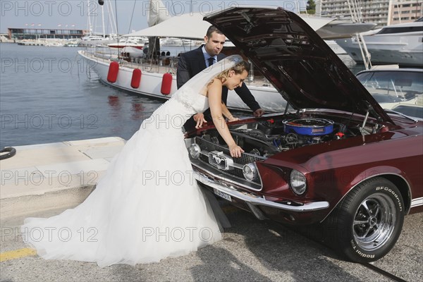 Bride and groom looking into the engine compartment of a Ford Mustang after a breakdown