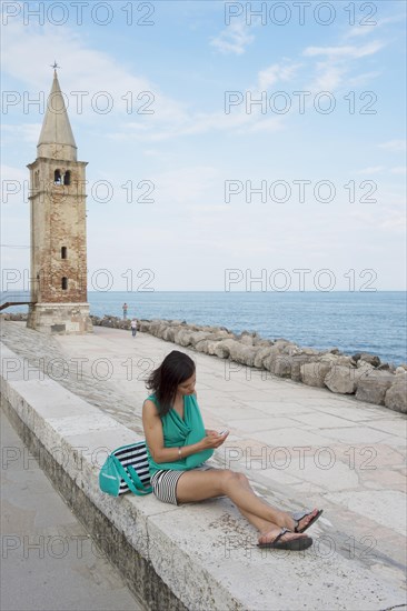 Woman with cell phone sitting on the wall in front of the church Madonna dell 'Angelo