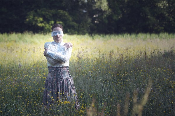 Woman with a lace mask in front of her eyes standing in a meadow