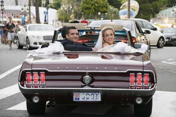 Bride and groom riding in an open Ford Mustang convertible car through the city