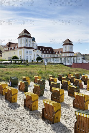 Roofed wicker beach chairs on the beach in front of the Kurhaus spa building