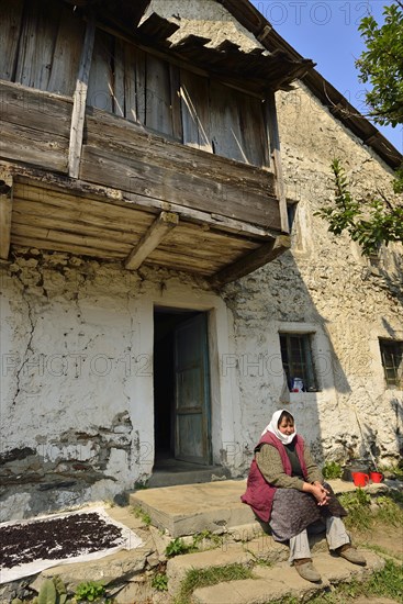 Albanian woman sitting in front of an old farmhouse