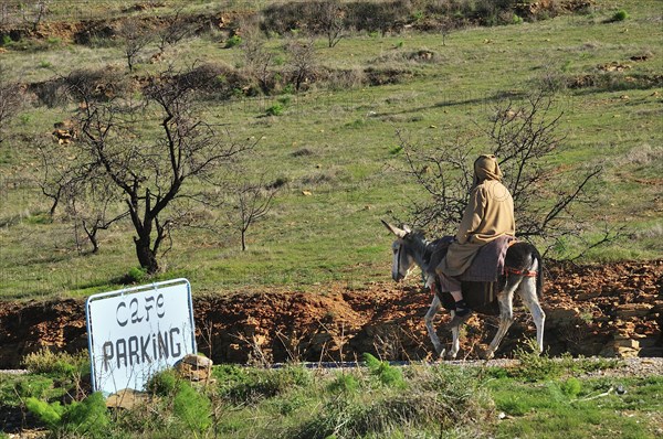 Man riding a donkey past a sign "Cafe parking"