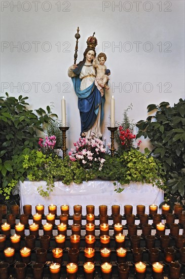 Sacrificial candles and a statue of Mary wearing a crown holding baby Jesus