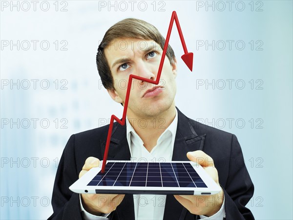 Businessman with a serious face holding an iPad with a plunging stock chart