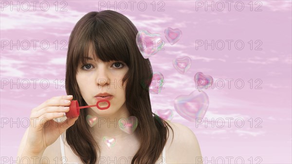 Young girl blowing heart-shaped soap-bubbles