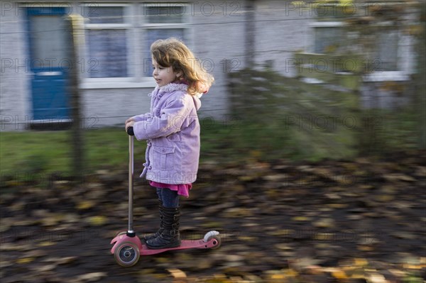 Four-year-old girl having fun riding a scooter