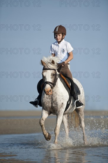 Girl on a pony trotting along the beach