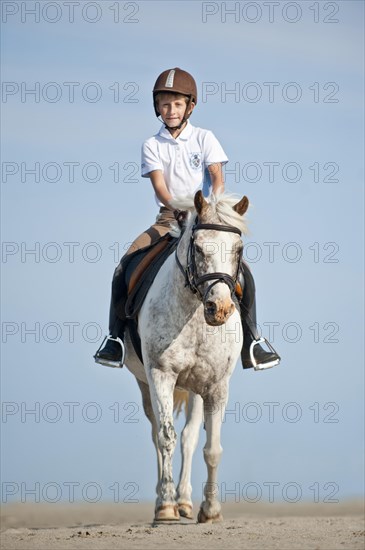 Girl riding a pony along the beach