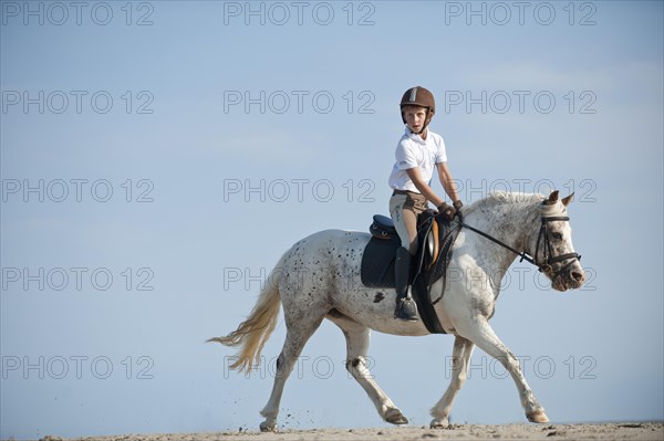 Girl on a pony trotting along the beach
