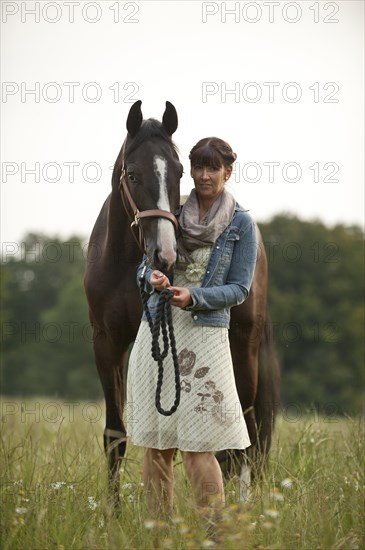 Woman standing beside a Hanoverian horse in a meadow