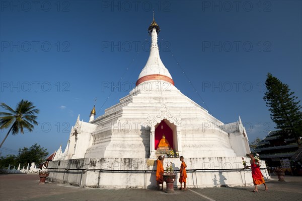 Young Buddhist monks with offerings in front of a Pagoda or Chedi