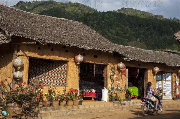 Woman riding a motorcycle in front of a tea shop in a village of the Chinese minority on the border with Myanmar