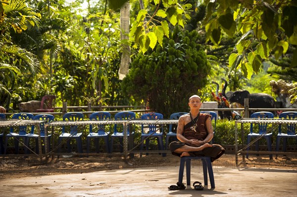 Praying or meditating Buddhist monk sitting on a plastic chair