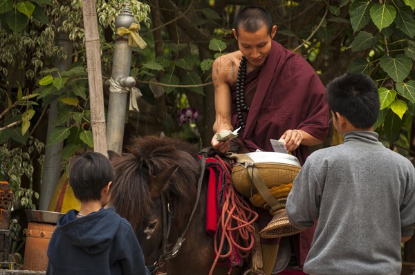 Buddhist monk on horseback with a begging bowl collecting alms in the morning