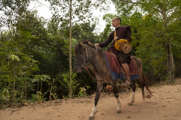 Buddhist monk on horseback with a begging bowl collecting alms in the morning