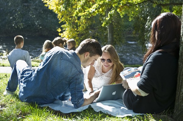 Students with a laptop and books on a meadow