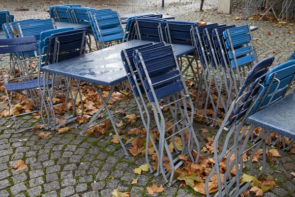 Empty tables and chairs of an outdoor dining in the rain with autumn leaves in the historic city centre of Cologne