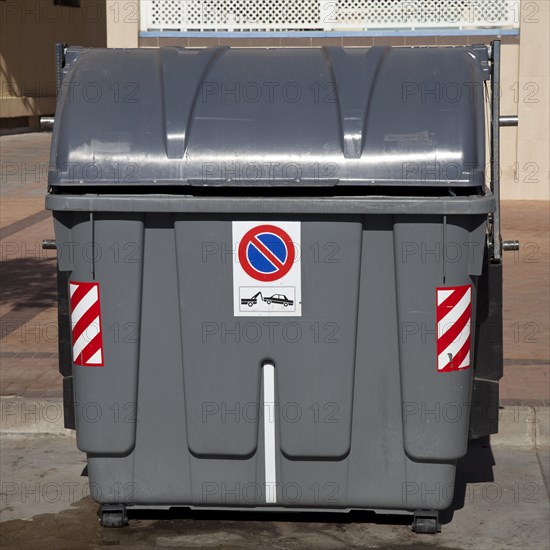 Wheeled trash can with a No parking sign standing on the roadside