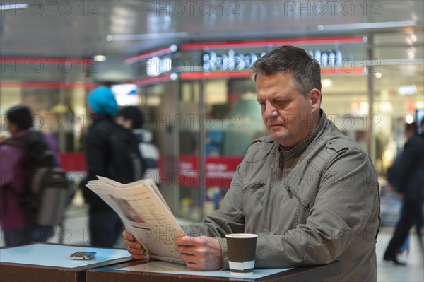 Man standing in a shopping mall reading a newspaper