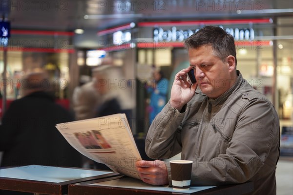 Man on a mobile phone reading a newspaper
