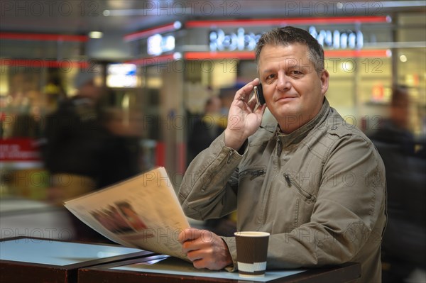 Man with a newspaper and a mobile phone in a shopping mall