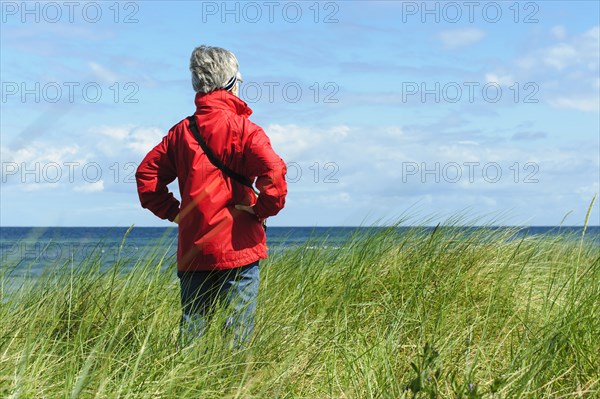 A woman standing in the dunes and looking out on the sea