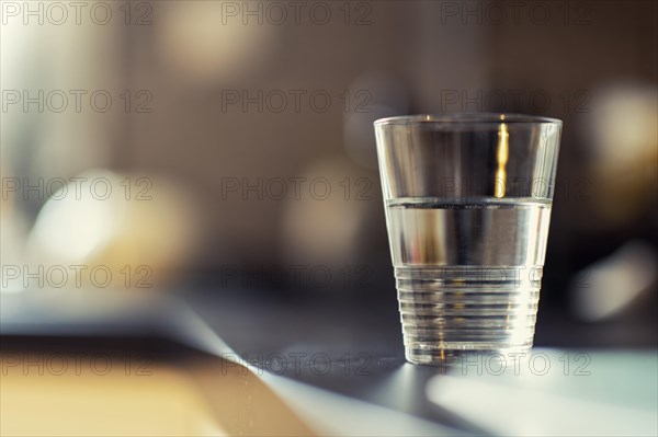 A half-full glass of water standing on a kitchen bench