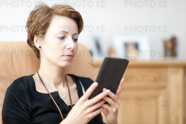 Young woman sitting in an armchair and reading an e-book