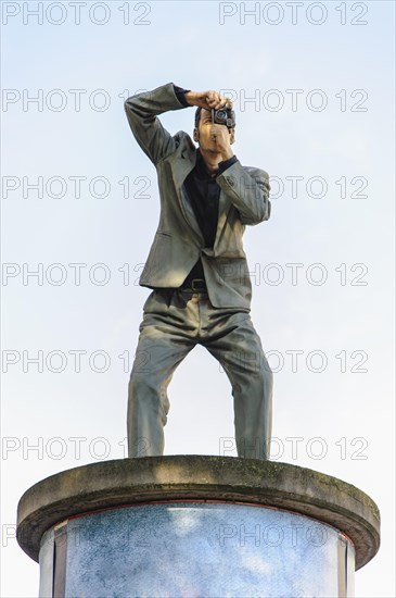 Sculpture of a man taking a photograph standing on an advertising column