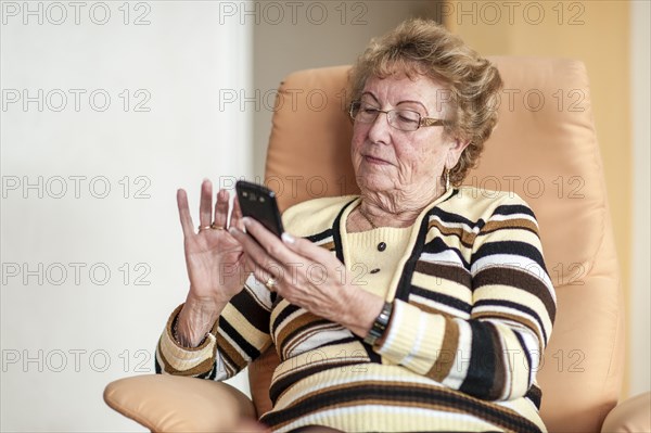 Elderly woman sitting in an armchair and using a smartphone