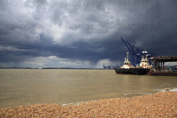 Tugboats moored at harbour of container port with passing rainclouds